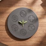 Somatic Rthyms Dark ceramic plate engraved with circular nature-inspired patterns, holding a small green sprout at its center, representing Somatic Rhythm offerings